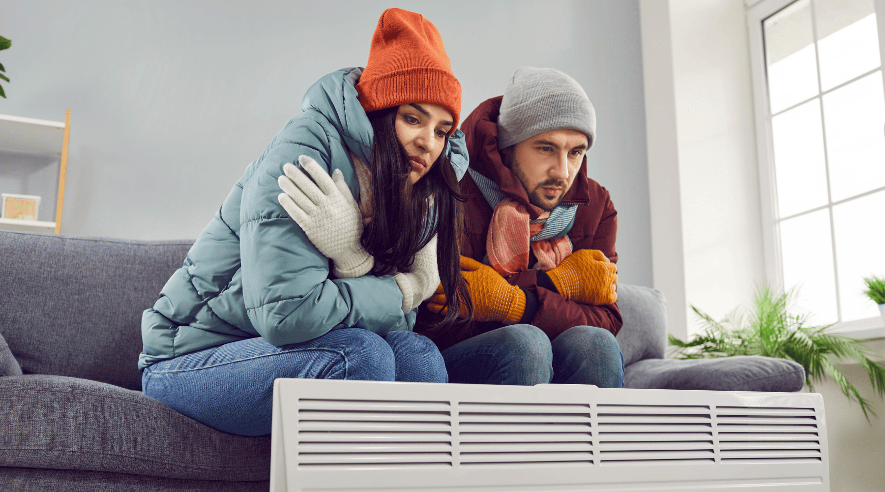 זוג אנשים יושב מול תנור חימום בבית קר עם מעילים וכובעי צמר - ברקע סלון | לייפסטייל